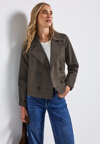 Dubbelknäppt jacka i mörkgrått tyg, med stora knappar, slagkrage och en avslappnad passform, parat med blå denimjeans.