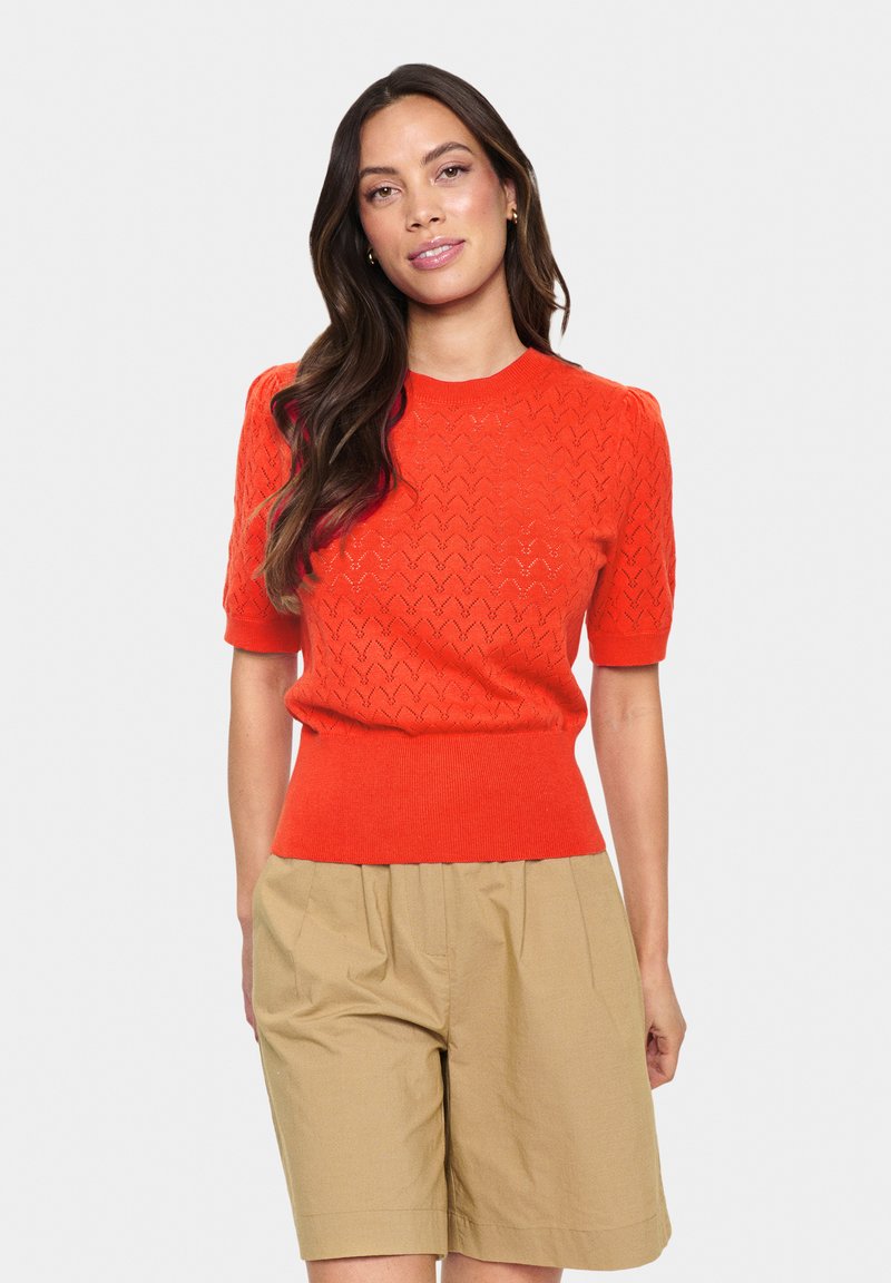 Klarorange kortärmad stickad topp med ett texturerat zigzagmönster och ribbad nederdel; matchad med beige shorts.