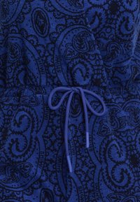 Mėlynos spalvos raštuota medžiaga su tamsiai mėlynu paisley raštu; apima juosmens juostą su atitinkamu virvės ir pakabukų komplektu. Minkšta tekstūra, vidutinio svorio medžiaga.