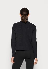 Pull en maille côtelée bleu marine avec col montant, coupe ajustée et manches raglan ; présente un tissu texturé et une taille élastique ajustée.