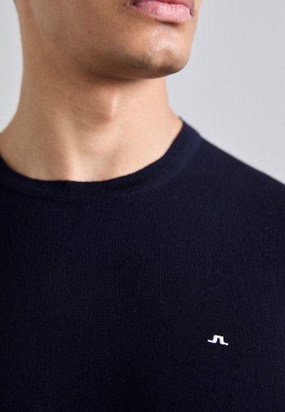 Navy-blauer Strickpullover mit Rundhalsausschnitt und kleinem weißen Logo auf der Brust, aus glattem, strukturiertem Stoff.