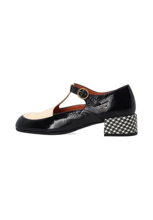 Black patent leather shoe with a beige toe cap, T-strap design, and a houndstooth patterned block heel. Features circular hardware detail.