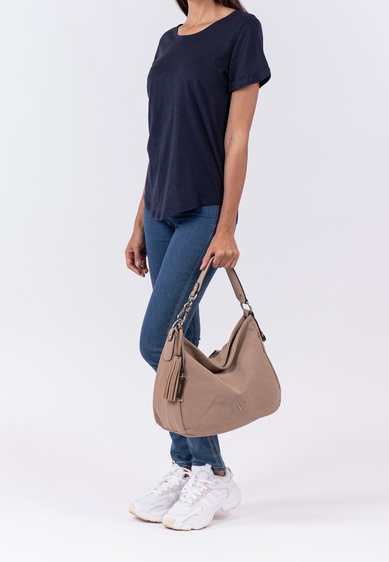 Femme portant un t-shirt bleu marine, un jean bleu, des baskets blanches, tenant un grand sac à main beige avec un détail pompon sur la sangle.