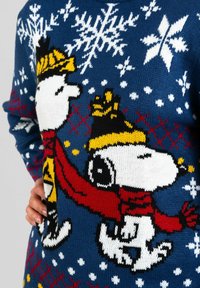 Maglione lavorato a maglia di colore blu scuro con personaggi di Snoopy che indossano una sciarpa rossa e una corona gialla, rifinito con fiocchi di neve bianchi e motivi geometrici rossi.