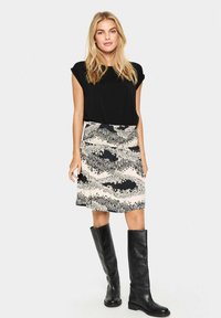 Haut noir à manches courtes, jupe genou à motifs crème et noire, associée à des bottes en cuir noir montantes. Texture lisse et coupe décontractée.