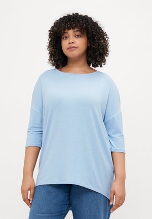 Top oversized de culoare albastru deschis, cu decolteu în formă de U, mâneci cu trei sferturi și textură moale, netedă. Purtați cu blugi albaștri.