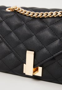 Borsa a tracolla nera trapuntata in pelle strutturata, con catena dorata e dettaglio di chiusura metallica rettangolare.