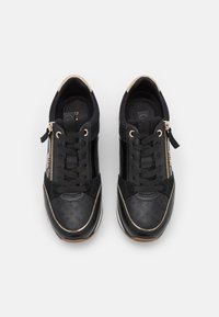 Svarta sportskor med en texturerad yta, som har guldaccenter, en sidoglasyr och snören. Släta och perforerade material används.