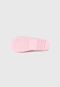 Semelle rose d'une chaussure avec un motif de texture et un petit logo en relief au centre, présentée sur un fond clair uni.