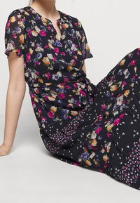 Blommig klänning med mörk bakgrund och flerfärgade blommor. Korta ärmar, nyckelhålsringning och en knytning i midjan. Utsvängd kjol.