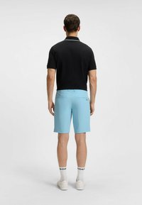 Polo nero con colletto bianco, abbinato a pantaloni corti azzurri chiari con tasche posteriori. Sneakers bianche e calzini con logo "BOSS".