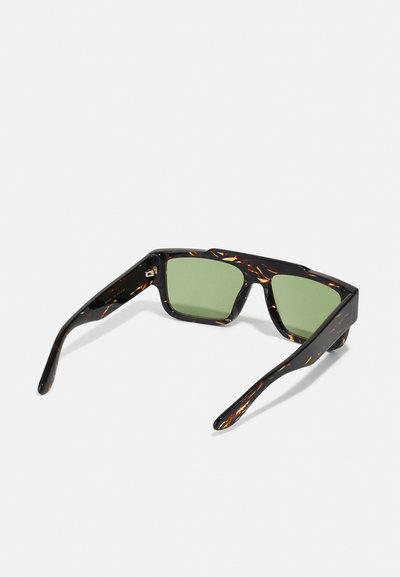 Gafas de sol carey con lentes verdes; montura gruesa y angular; textura suave; acentos distintivos de patrones claros y oscuros.