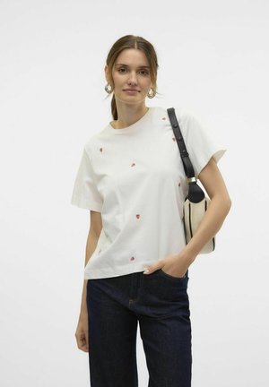 T-shirt en coton blanc avec une petite broderie de fraise rouge, coupe décontractée, col rond, assorti à un jean bleu foncé et un sac beige.