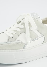 Sneaker featuring a white leather and grey suede upper, flat white laces, silver accents, and a thick white sole with a textured design.