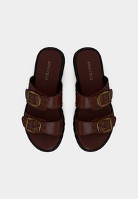 Sandales en cuir marron avec deux boucles dorées réglables et de petits clous décoratifs sur des semelles noires, vues de dessus.