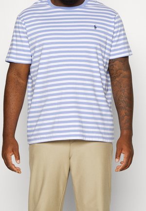 Man wearing a light blue and white striped short-sleeve shirt and beige pants, with a tattoo on the right arm visible.