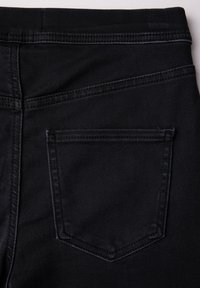 Svarta denimjeans med en bakfickan som har en spetsig klaff, synliga sömmar och en slät textur. Inga dekorationer eller mönster.