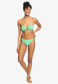 Zelené bikiny s bandeau vrchom a stredovým krúžkom, s nastaviteľnými bočnými viazaním, vyrobené z hladkého, elastického materiálu.