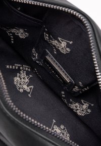 Interno della borsa in pelle nera con fodera blu navy decorata con ripetuti loghi di giocatori di polo bianchi, cerniera argentata e una piccola etichetta con del testo.