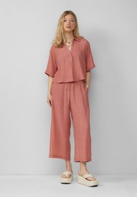 Roodbruine, gestreepte, lichte top met knoopsluiting en opgerolde mouwen, gecombineerd met bijpassende wijde broek. De plateau-sandalen zijn crème.