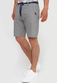 Gråstribede shorts lavet af stof, med en marineblå snor, forlommer og et brunt accentmærke. Båret med hvide sneakers.