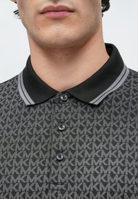 Šedé vzorované polo tričko se černým límečkem se šedými pruhy, třemi knoflíky vpředu a výrazným designem loga.