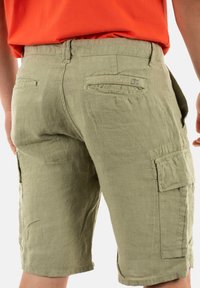 Pantalones cortos de carga color verde oliva con un tejido texturizado, bolsillos laterales y un corte relajado, que terminan justo por encima de la rodilla con un dobladillo cosido.