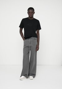 Camiseta de algodón negra con el texto "ORIGINAL", combinada con unos jeans gris de tiro alto y pierna ancha y zapatillas blancas. Diseño minimalista, detalles sencillos.
