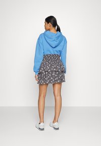 Hoodie azul de algodão com uma textura suave, combinado com uma saia rodada preta com padrão floral. Apresenta uma cintura elástica, usada com ténis brancos.