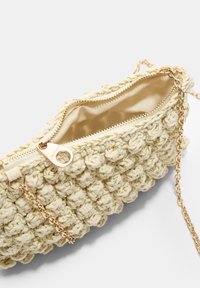 Beige, tkaná taška s texturovaným, nadýchaným designem; obsahuje zlatý zip a řetízek; vnitřek podšitý měkkou tkaninou.