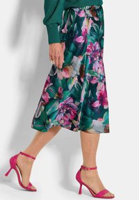 Blumenmidirock in Grün, Pink und Blau mit einem fließenden Design; kombiniert mit knallpinkfarbigen High-Heels.
