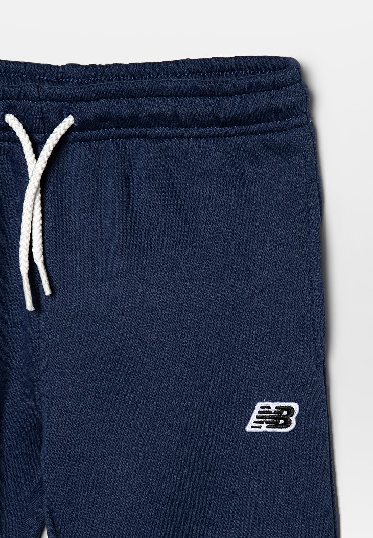 Pantalons de survêtement bleu marine avec cordon blanc et logo New Balance brodé près de la poche gauche.