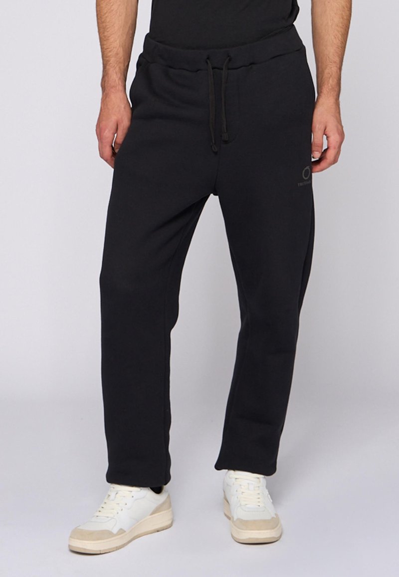 Czarne dresy wykonane z miękkiego materiału, z elastycznym pasem i sznurkiem, bocznymi kieszeniami oraz lekko zwężającym się krojem nogawek.