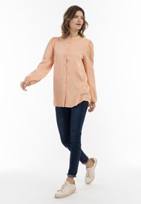 Persikofärgad blus med långa puffärmar och knäppning framtill, ihop med mörkblå tajta jeans och ljusa sneakers.