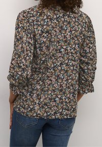 Blus med blommönster på mörk botten, flerfärgade blommor, puffärmar och avslappnad passform. Matchas med figursydda blå jeans.