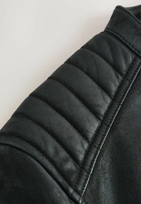 Zwart leren motorjackmouw met gewatteerde padding, een gladde textuur en gedetailleerde stiksels langs de naad.