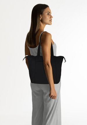 Zwarte tote bag met schouderbanden, gemaakt van duurzaam stof. Rechthoekige vorm, heeft een rits en een buitenvak. Glad oppervlak.