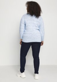 Hellblauer Strickpullover mit horizontalen Streifen, langen Ärmeln und lockerem Schnitt, kombiniert mit dunkler Jeans und weißen Sneakern.