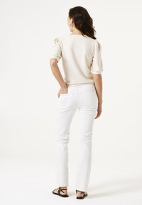 Haut beige à manches bouffantes associé à un jean blanc à jambe droite et des sandales noires. Le haut a une texture lisse et une coupe décontractée.