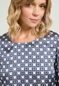 Bluse med geometrisk mønster i nuancer af grå og hvid; har rund halsudskæring og letvægtsmateriale.