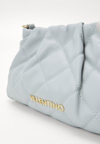 Jasnoniebieska pikowana torebka ze skóry z złotym logo "VALENTINO". Charakteryzuje się miękką, teksturowaną powierzchnią i zaokrąglonym kształtem.