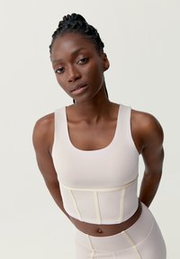 Světlý béžový sportovní podprsenka s čtvercovým výstřihem, silnými popruhy a kontrastním krémovým prošíváním. Přiléhavý střih a zkrácená délka.
