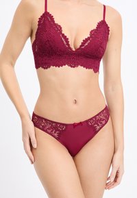 Bralette in pizzo bordeaux e perizoma abbinato, con bordi a scallop, motivo floreale e piccolo fiocco decorativo sul perizoma.