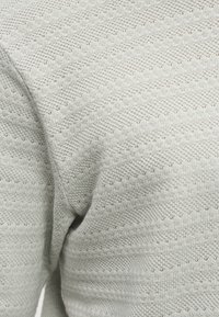 Κοντινό πλάνο υφάσματος πλεκτού σε ανοιχτό γκρι χρώμα με διακριτικό ζιγκ ζαγκ μοτίβο και υφή ύφανσης.