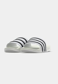 Λευκά σανδάλια με λευκή σφήνα και τρεις μαύρες ρίγες στο πάνω μέρος. Κατασκευασμένα από υλικό με υφή, με καμπυλωτή λευκή σόλα και μινιμαλιστικό σχέδιο.