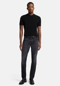 Svart kortärmad t-shirt kombinerad med åtsittande mörkgrå jeans. Outfitten har ett texturerat svart bälte med en rund spänne och svarta skor.