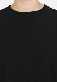 T-shirt noir à col ras du cou en tissu texturé, avec un décolleté lisse et une apparence générale uniforme.