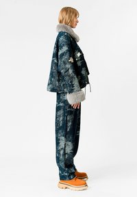 Chaqueta de gran tamaño, texturizada en azul, con cuello de piel de oveja gris, combinada con pantalones a juego y zapatos de plataforma naranjas. Incluye acentos de parches.