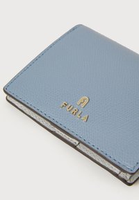 Portafoglio in pelle blu chiaro con superficie testurizzata, hardware dorato con logo "Furla" e fodera interna a contrasto. Forma rettangolare compatta.