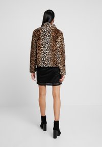 Leopardmønstret faux fur jakke med høj krave, brune og sorte mønstre, parret med en sort plisseret nederdel og sorte hæl ankle boots.